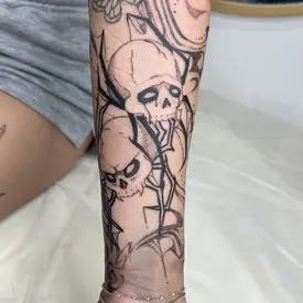 a black fineline tattoo of two skulls and jagged lines running up a person's arm